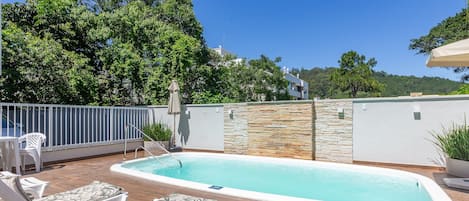 A swimming pool with lounge chairs, a stone wall, and a view of the surrounding greenery.