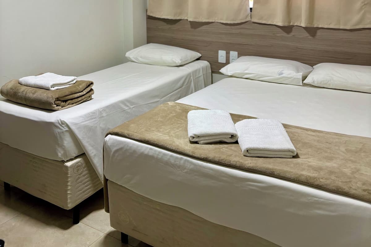 Habitación de hotel con dos camas, cortinas color beige, ropa de cama blanca y una lámpara en el techo.