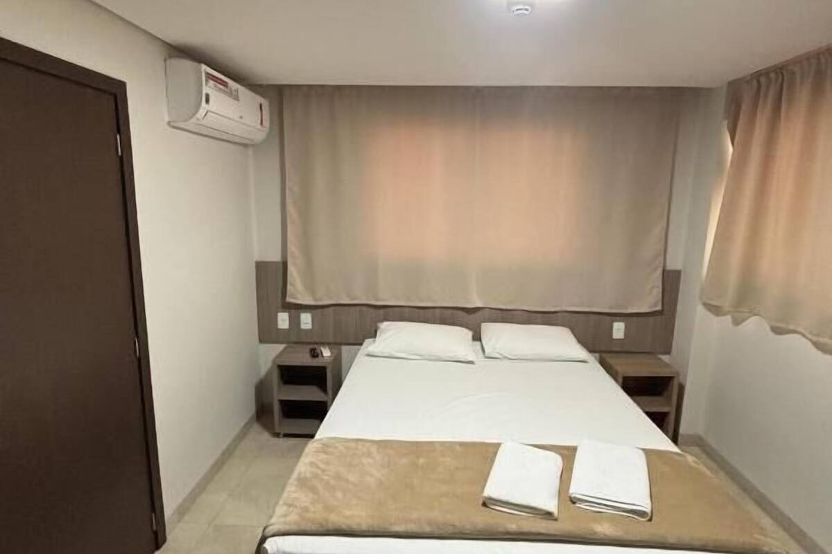 Una habitación de hotel con cama, mesitas de noche, un armario y aire acondicionado.