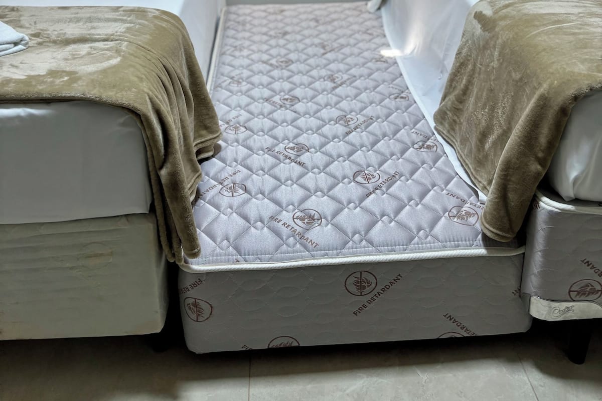 Habitación compacta con dos camas, colchones acolchados y cabecero con interruptor de luz.