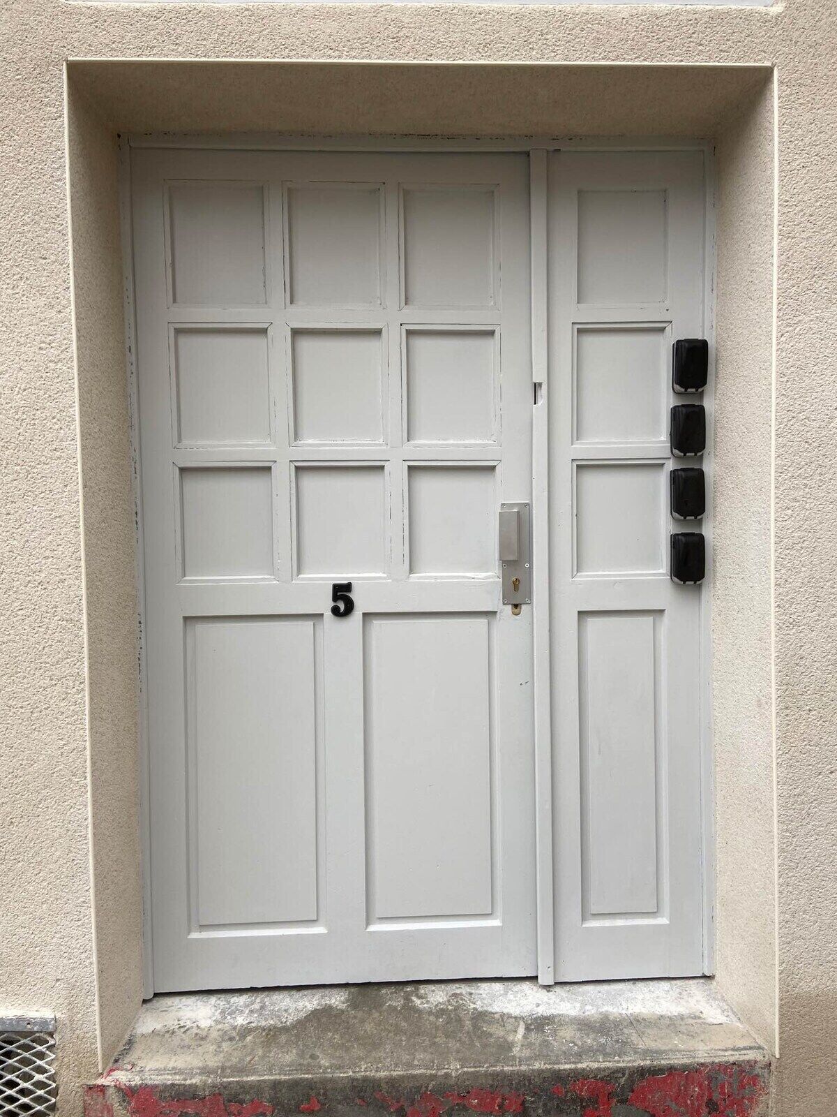 Une porte blanche à deux battants, portant le numéro « 5 » et munie d’une fente pour le courrier sur le côté droit.