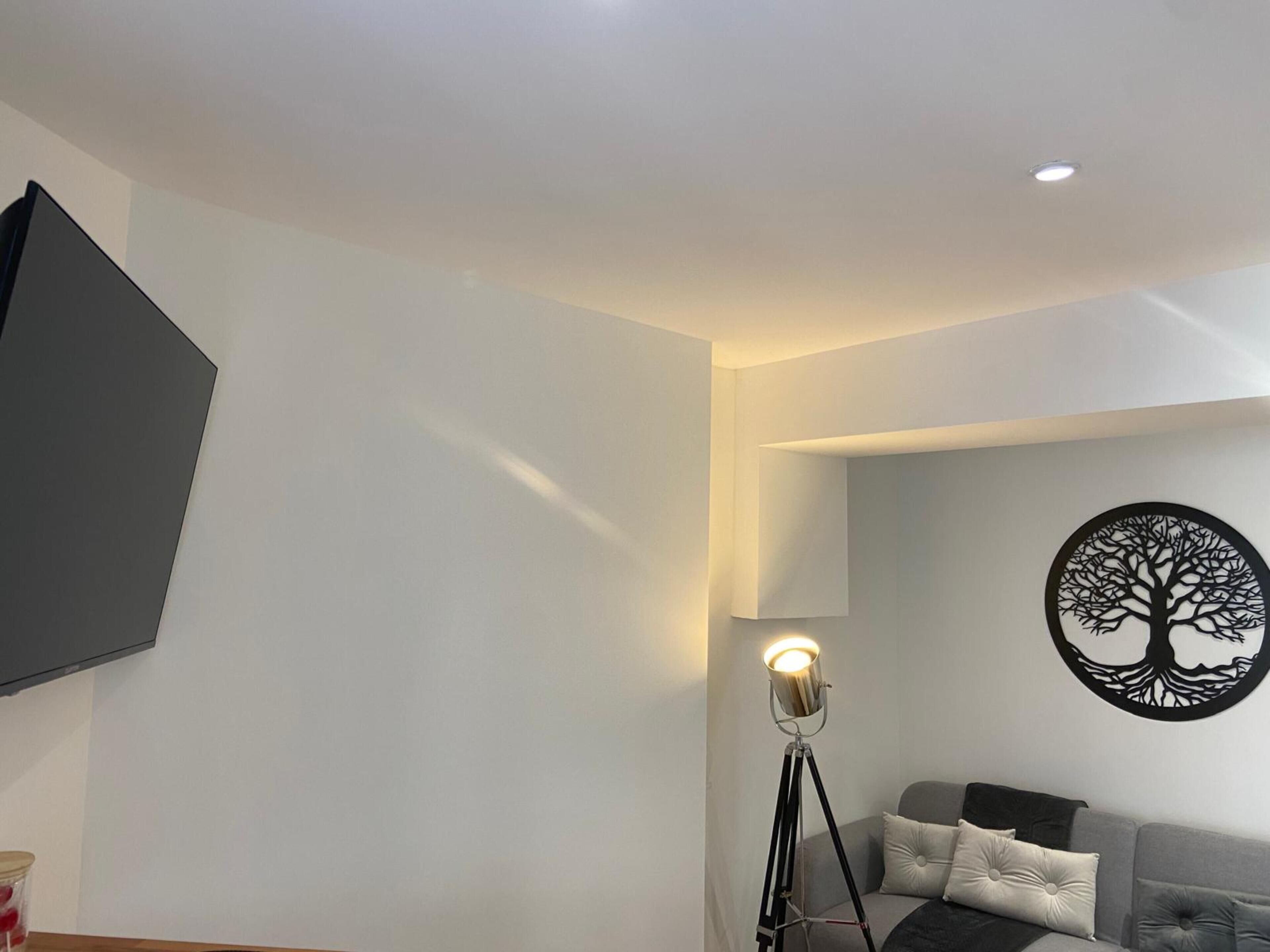 Ein modernes Wohnzimmer mit einem grauen Sofa, einer Stehlampe und einem an der Wand befestigten Fernseher.
