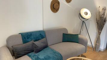 A grey sofa with teal and dark grey cushions, a woven basket, and a floor lamp with a light bulb.