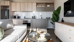 A modern kitchen with wooden cabinets, a built-in oven, and a dining area with a glass table and white bowl. - Century City Escape | Walk to Shops and Views (Cape Town)