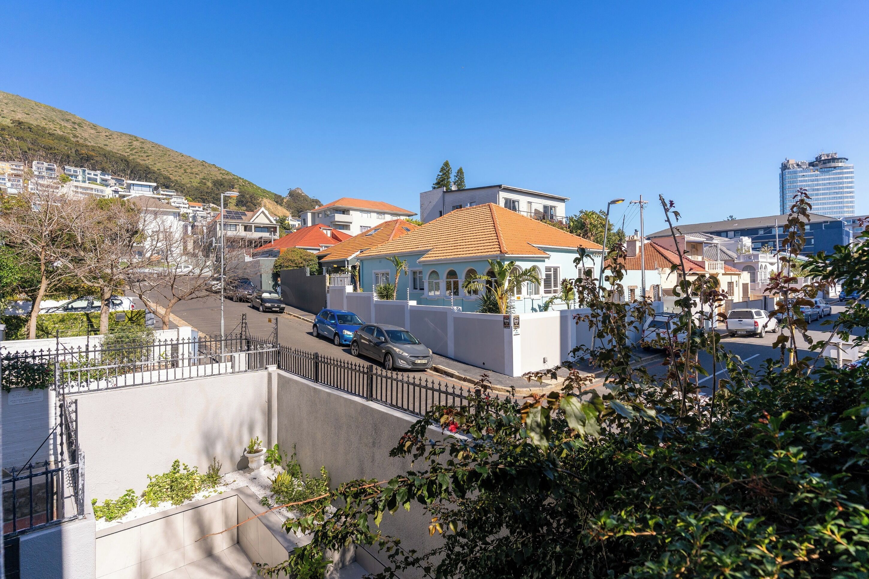 A residential area with modern houses, a street with cars, and a hill in the background.