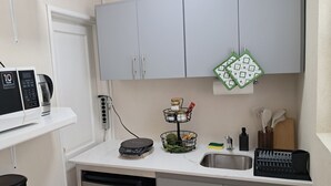A compact kitchen with grey cabinets, a white countertop, a coffee maker, a dish rack, and a sink.