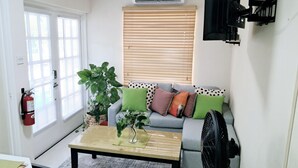 A living room with a sofa, a coffee table, a potted plant, a fire extinguisher, and a wall-mounted fan.