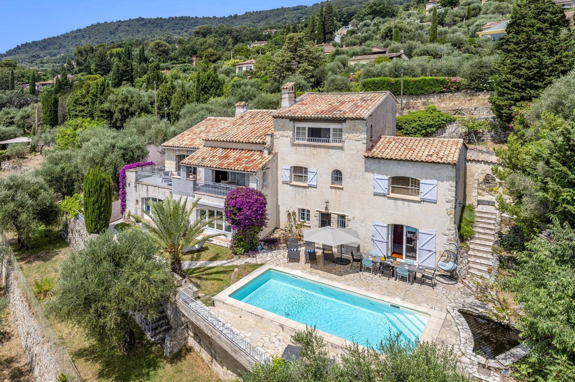 A two-story villa with a swimming pool, surrounded by lush greenery and hills.