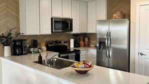 A modern kitchen with white cabinets, stainless steel appliances, and a central island with a bowl of snacks. - Lackland Air Force Base at 9 min-Brauning Lake at 25 min-3 bdr-King size-Grill (Von Ormy)