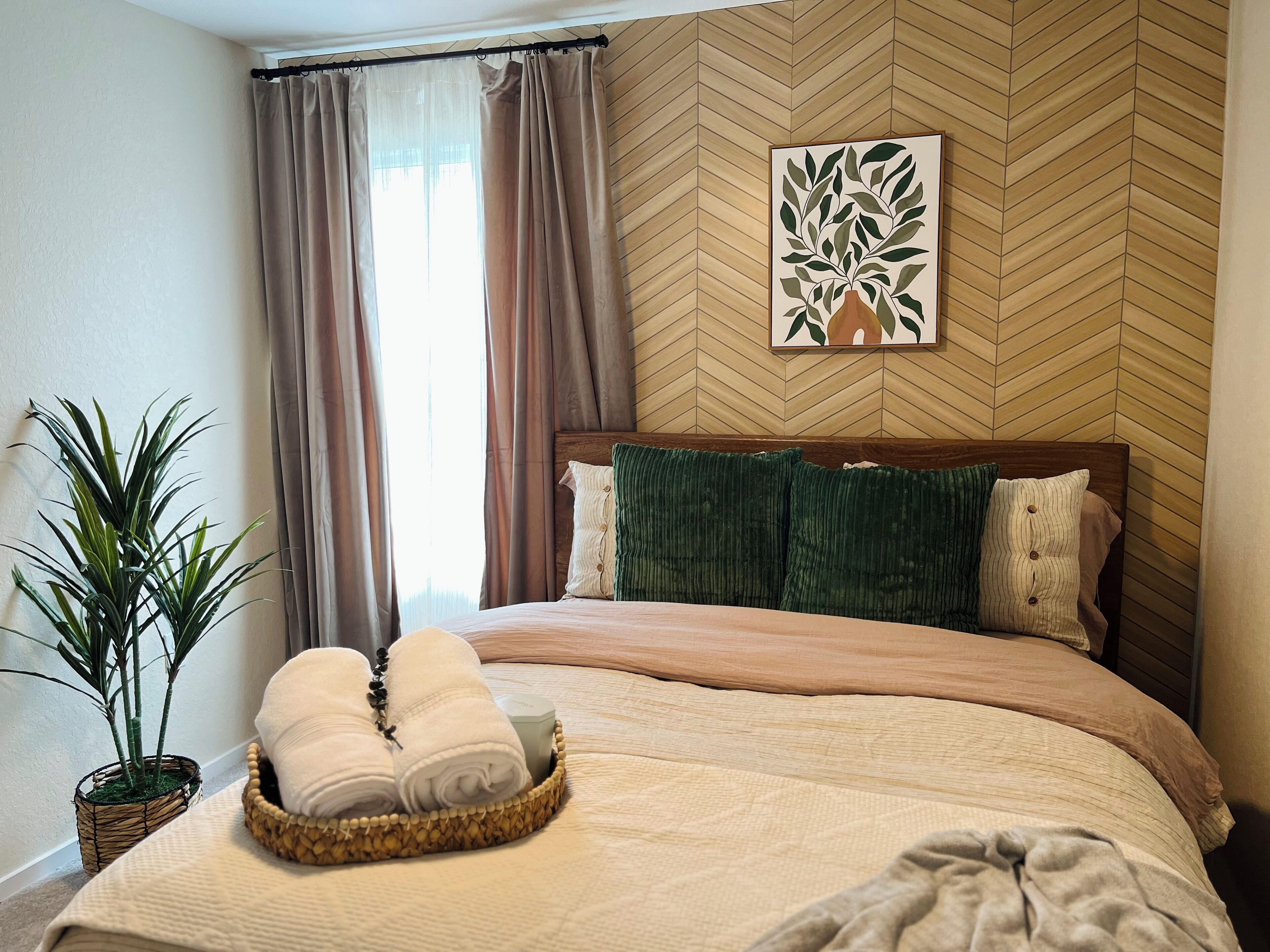 Een keurig opgemaakt bed met een hoofdeinde, een kamerplant en een mand met handdoeken.