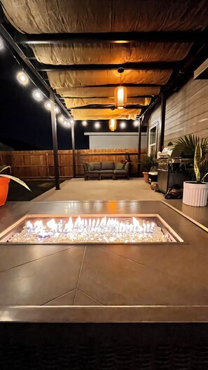 A covered outdoor patio with a fire feature, seating, and potted plants.