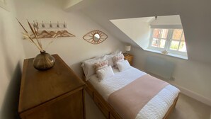Ein Schlafzimmer mit einem Bett, einem Nachttisch aus Holz, einem Spiegel und einem Fenster.