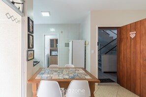 A dining area with a wooden table and white chairs, a refrigerator, and a kitchen in the background. - Apartment w/ Barbecue 450m From the Beach Rci0201 (Florianópolis)