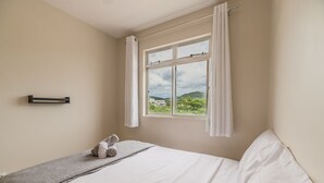 A bedroom with a bed, a window with curtains, a towel on the bed, and a wall-mounted towel rack.