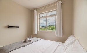 A bedroom with a bed, a window with curtains, a towel on the bed, and a wall-mounted towel rack. - Apartment w/ Barbecue 450m From the Beach Rci0201 (Florianópolis)