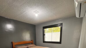 Een slaapkamer met een enkel bed, een raam en een airconditioning.