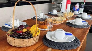 Een houten eettafel gedekt met borden, glazen en een mand met fruit.