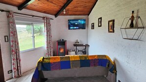 A cozy room with a wooden ceiling, a bed with a colorful quilt, a television on the wall, and a window with floral curtains. - Brand new! Charming corner in the sierras (Marmarajá)