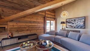 A cozy living room with a wooden ceiling, a grey sofa, a round coffee table, and a painting on the wall. - New Agora 202 Duplex | Central close to the slopes (Les Gets)