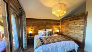 A bedroom with a large bed, wooden walls, and a hanging light fixture. - New Agora 202 Duplex | Central close to the slopes (Les Gets)