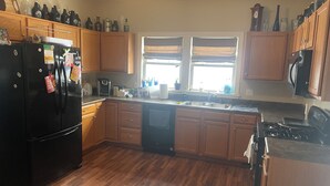 Una cocina con armarios de madera, un refrigerador negro, una estufa y una ventana con persianas.