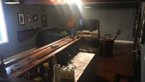 Una zona de bar con mostrador de madera, botellas y un televisor al fondo.