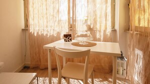 Une pièce avec une table et des chaises, une fenêtre avec des rideaux légers et un lit.