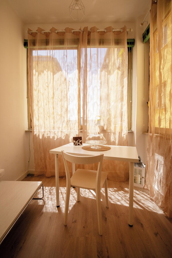 Una habitación con una mesa, sillas, una ventana con cortinas traslúcidas y una cama.