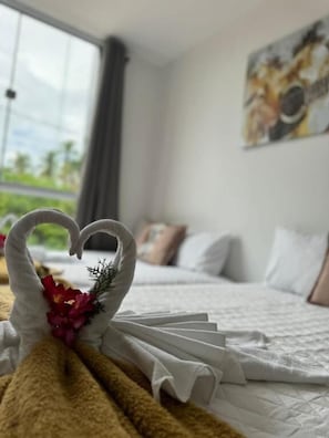 A neatly made bed with a heart-shaped towel decoration and a bouquet of flowers. - Hercules Beach Paradise (Maragogi)