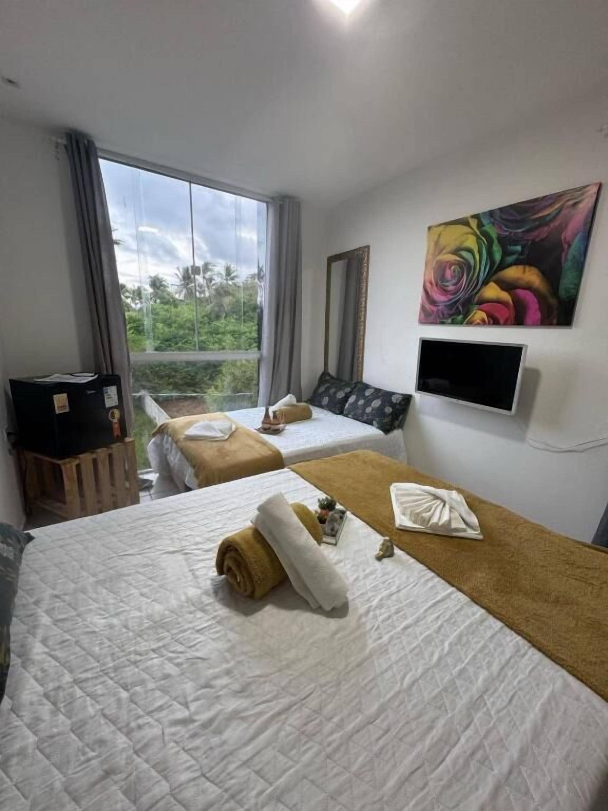 A hotel room with two beds, a TV, a painting, and a window with a view.