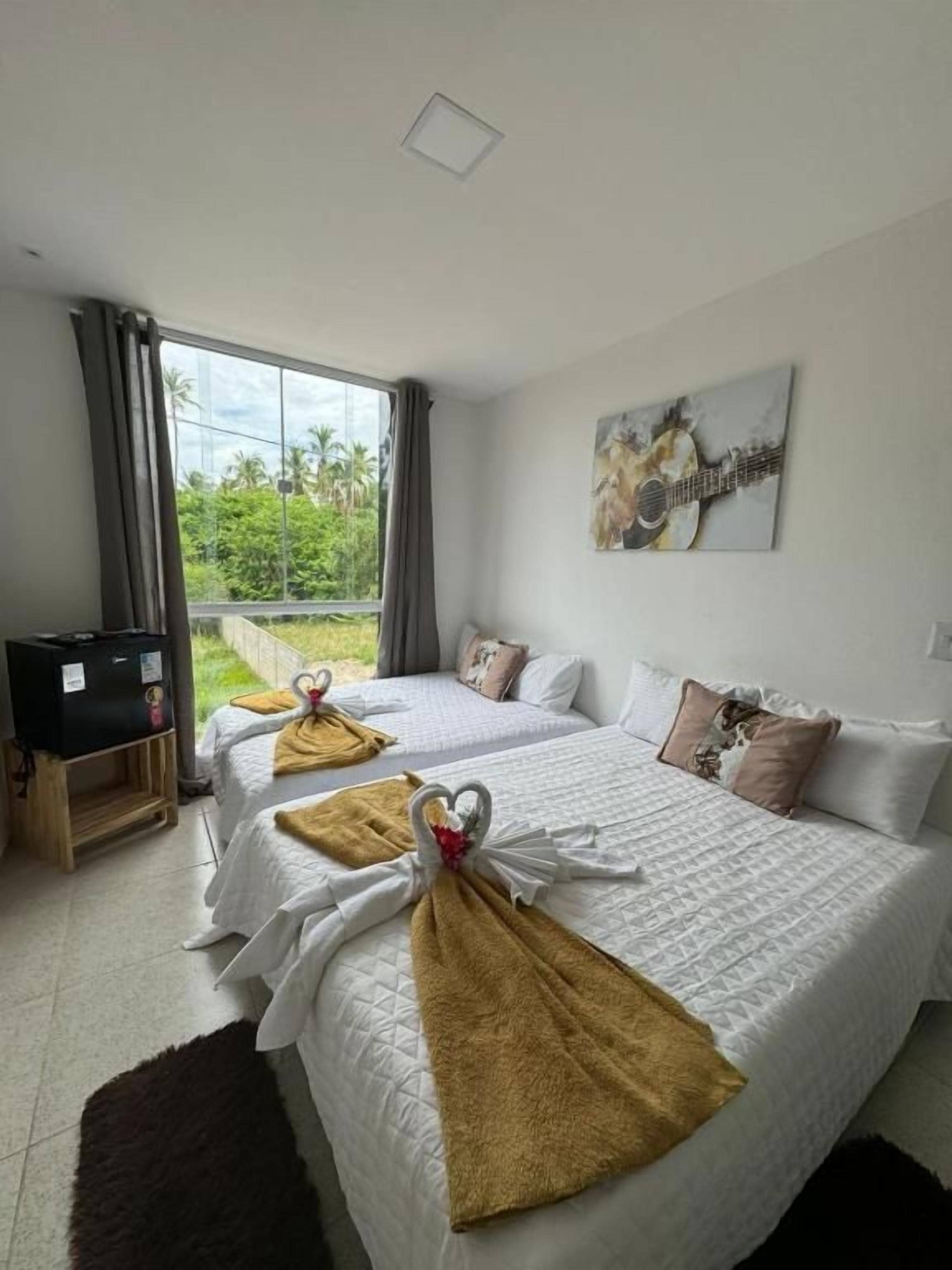 A hotel room with two beds, a television, a painting, and a view of greenery outside.