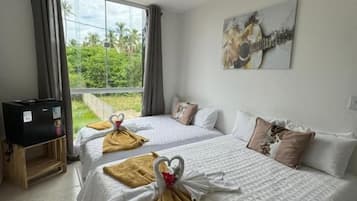 A hotel room with two beds, a television, a painting, and a view of greenery outside.
