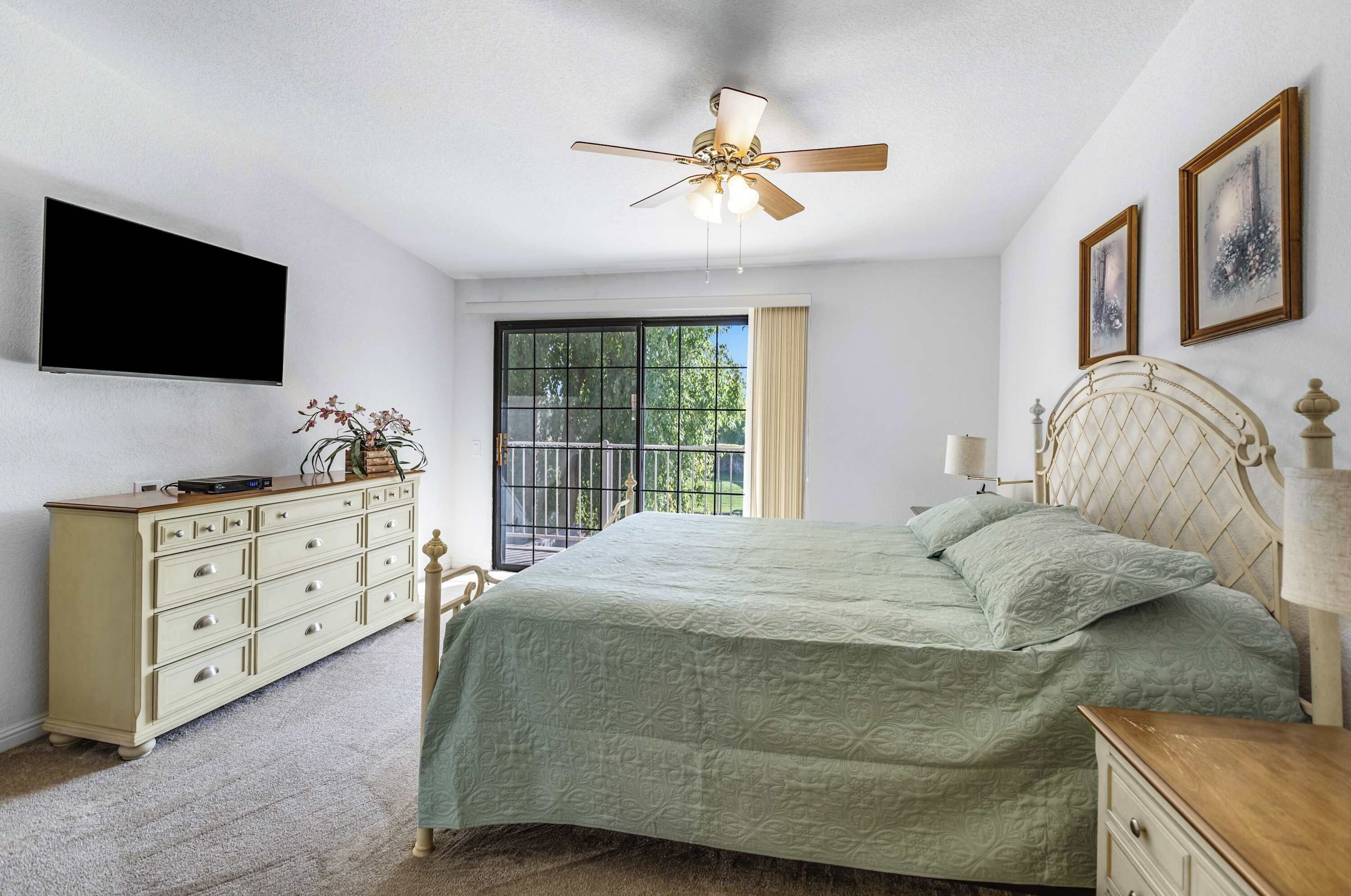 A bedroom with a bed, a dresser, a ceiling fan, a TV, and a window with curtains.