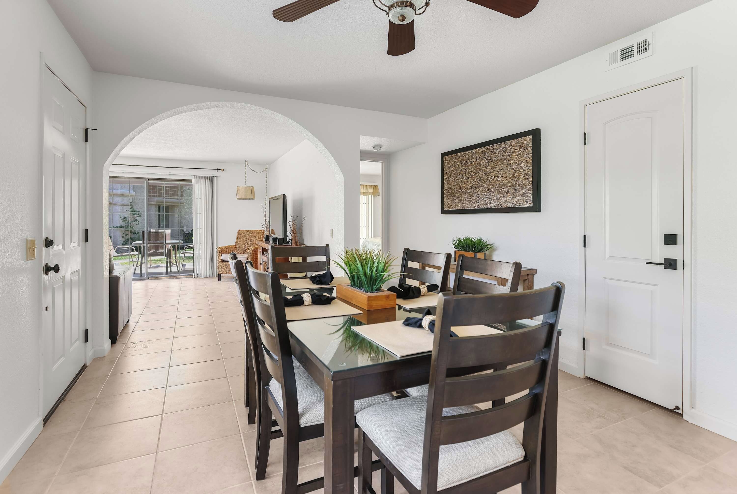 A dining area with a glass-top table, dark wooden chairs, and a ceiling fan.