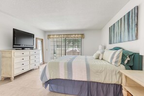 A bedroom with a bed, a dresser, a television, and a window with blinds.