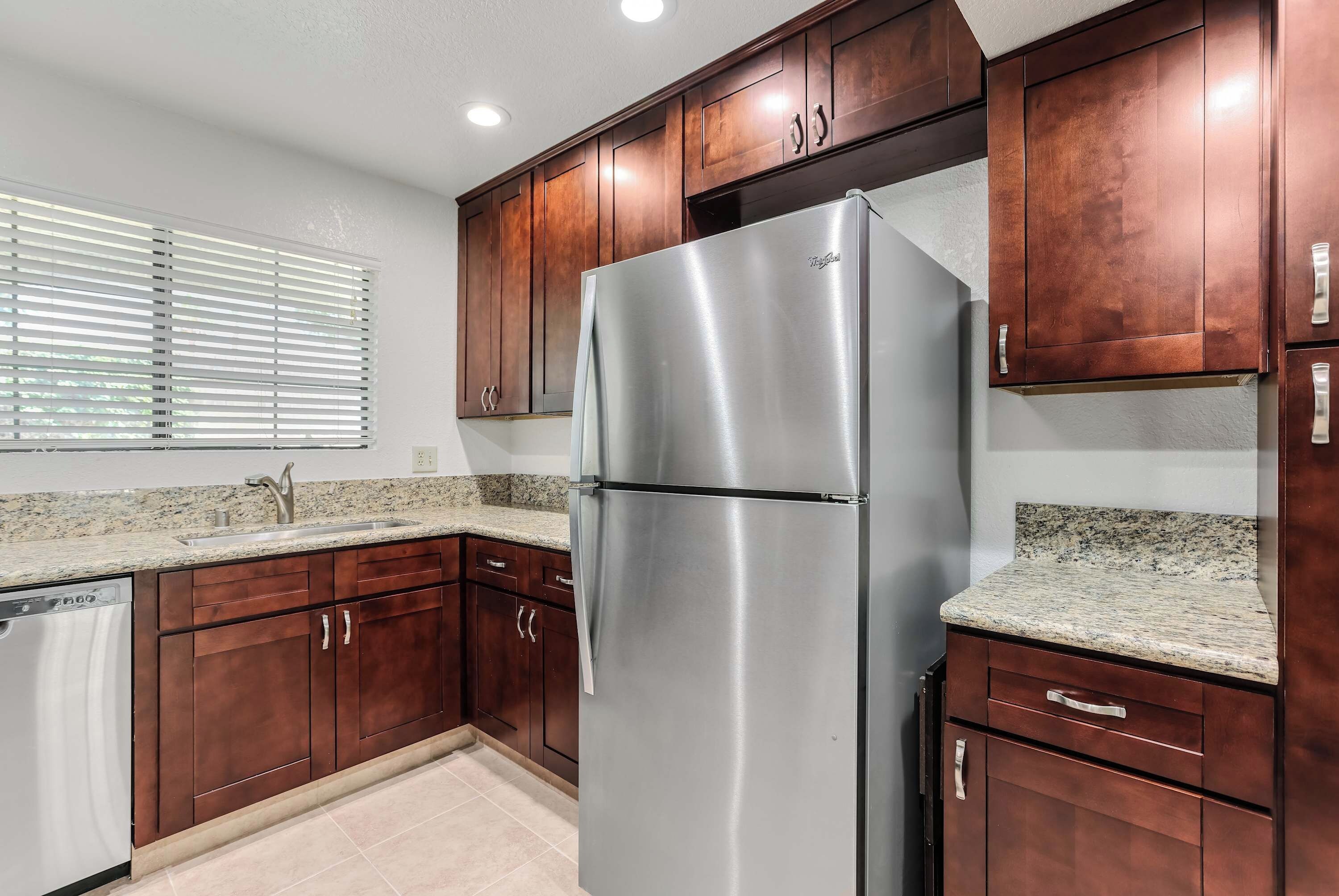 A kitchen with wooden cabinets, a stainless steel refrigerator, granite countertops, and a dishwasher.
