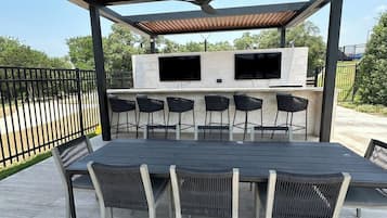 Eine Terrasse im Freien mit Grill, Sitzgelegenheiten und einem an einer Steinmauer befestigten Fernseher.