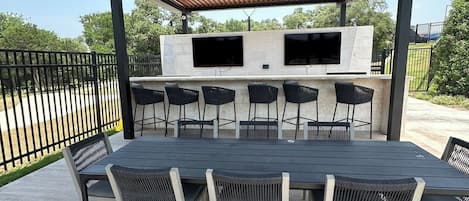 An outdoor patio with a grill, seating, and a TV mounted on a stone wall.