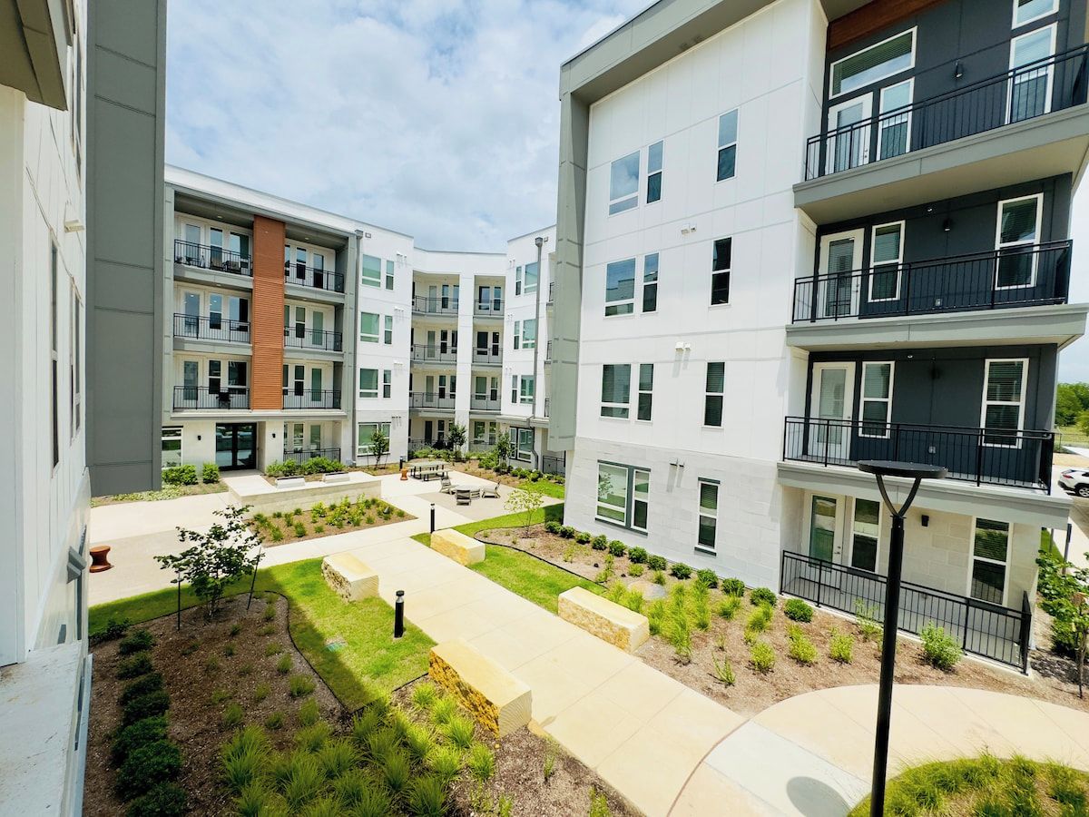 A multi-story residential building with balconies, a courtyard with seating, and a well-maintained garden.