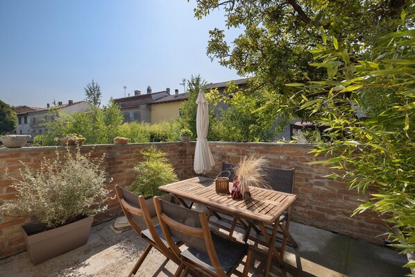 A patio with a wooden table and chairs, surrounded by potted plants and a brick wall.