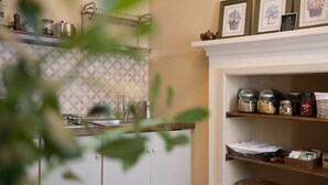 A kitchen with a patterned backsplash, a sink, a drying rack, and shelves with jars and kitchen items.