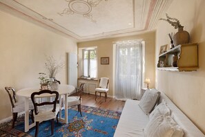 Ein Zimmer mit Esstisch, Stühlen, einer Couch, einem gemusterten Teppich und einem dekorativen Regal.