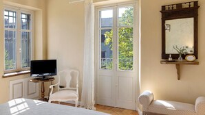 Habitació amb llit, cadira, televisió, finestra amb cortines i mirall a la paret.