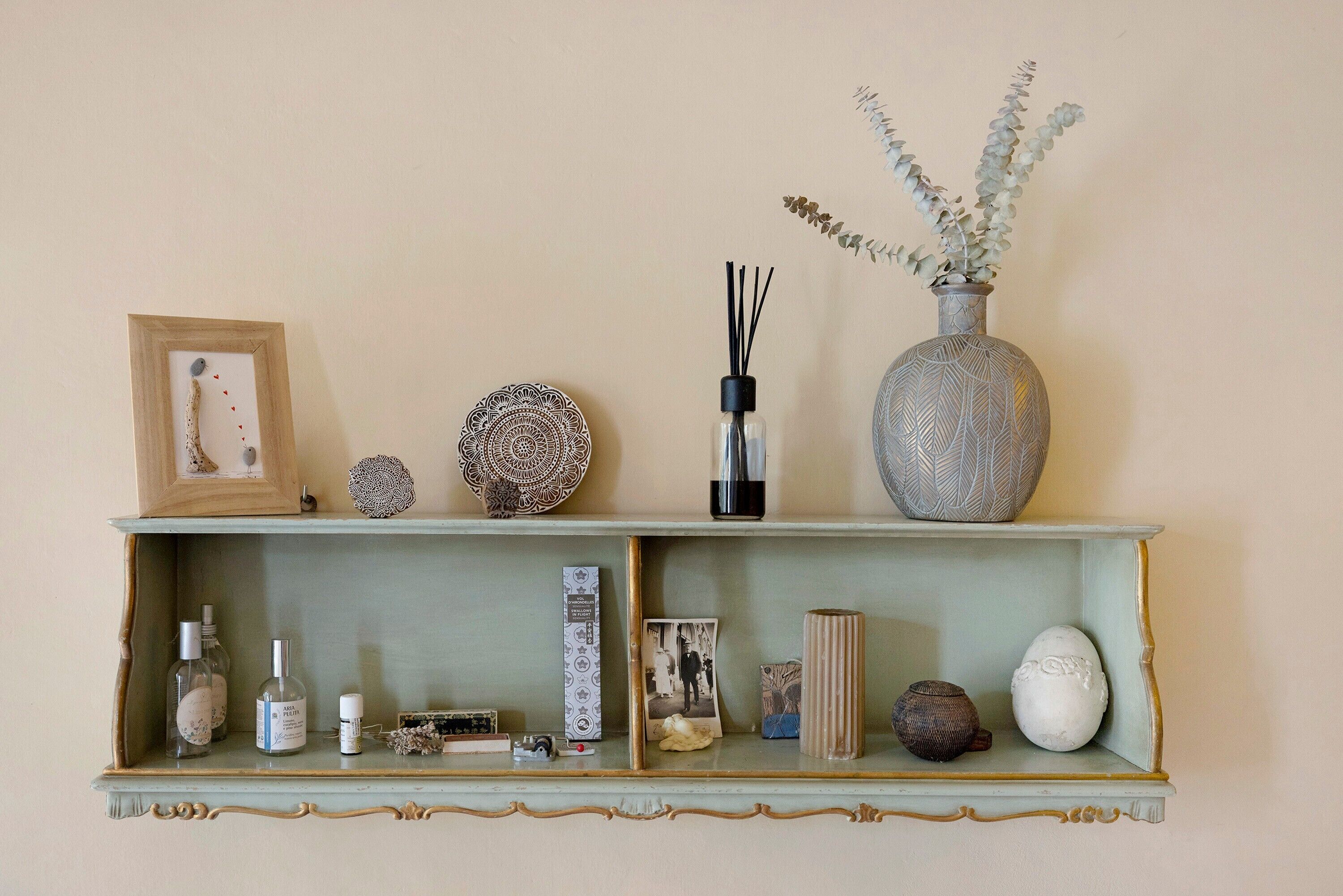 Een plank met decoratieve objecten, waaronder een ingelijste foto, een decoratieve kom, een fles, een vaas met planten en diverse kleine voorwerpen.