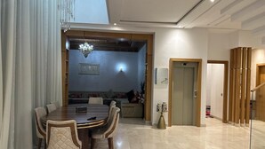Zona menjador moderna amb una taula rodona i cadires, una làmpada penjant i vista cap a un saló amb un sofà i objectes decoratius.