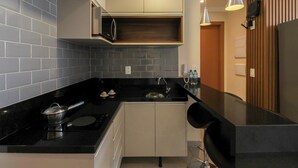 A modern kitchen with black countertops, white cabinets, and a microwave. There are two pendant lights above the sink and a wooden panel on the right wall.