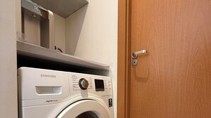 A Samsung digital-inverter washing machine in a laundry room with a wooden door and a white tiled floor.