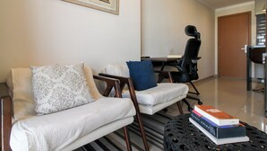 A living room with a sofa, a chair, a coffee table with books, a desk, and a framed picture on the wall.