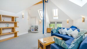 A spacious loft with a high ceiling, a blue sofa, wooden shelves, and a skylight.