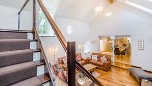 A spacious living area with a wooden staircase, a dining area, and a kitchen visible through an open door.